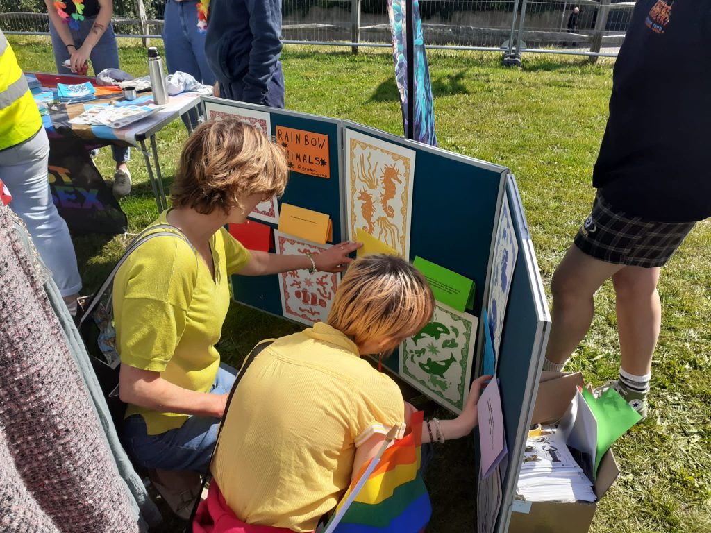 Two people crouching down inspecting some illustrated prints of rainbow animals and the facts that go with them on a display