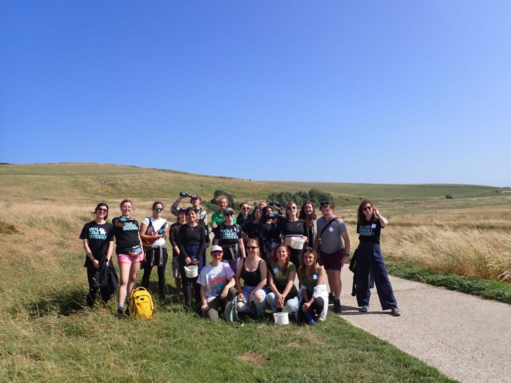 A group of around 30 attendees and the wild coast sussex team stand smiling in front of grassy hills and a blue sky