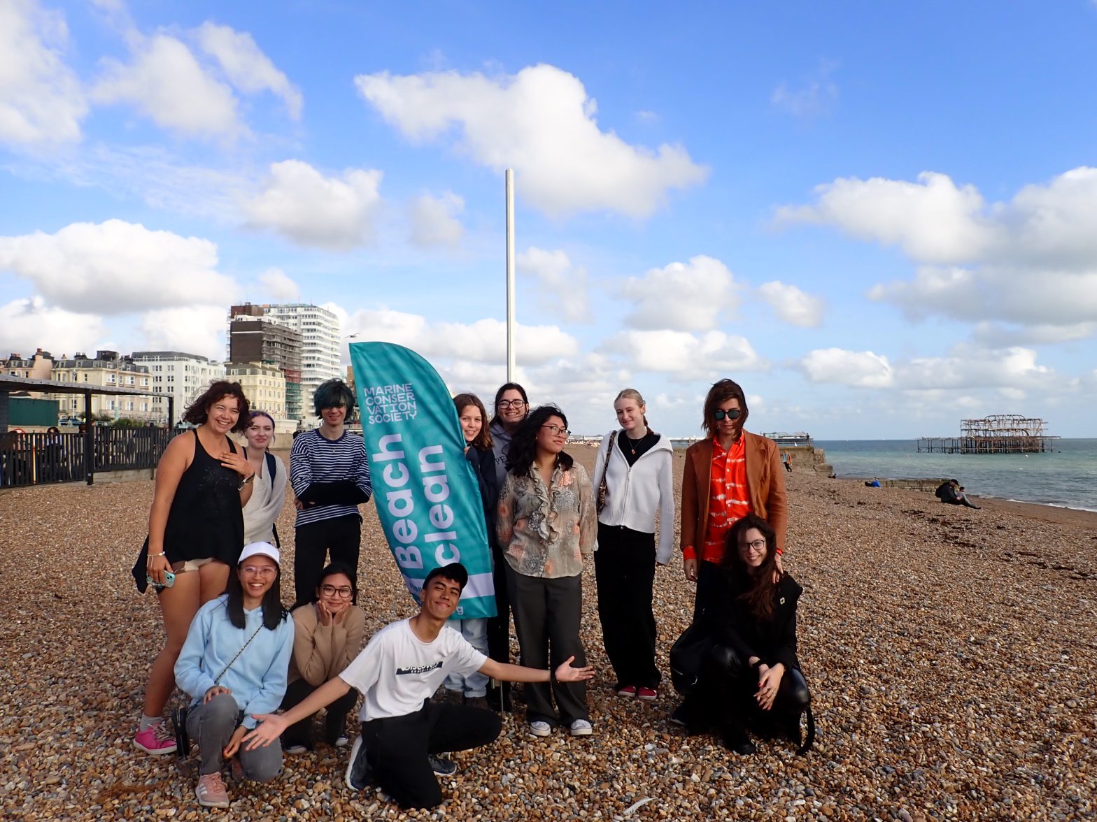 Group of beach clean attendants standing in a group on the beach smiling with the beach clean flag. the brighton west pier is in the background